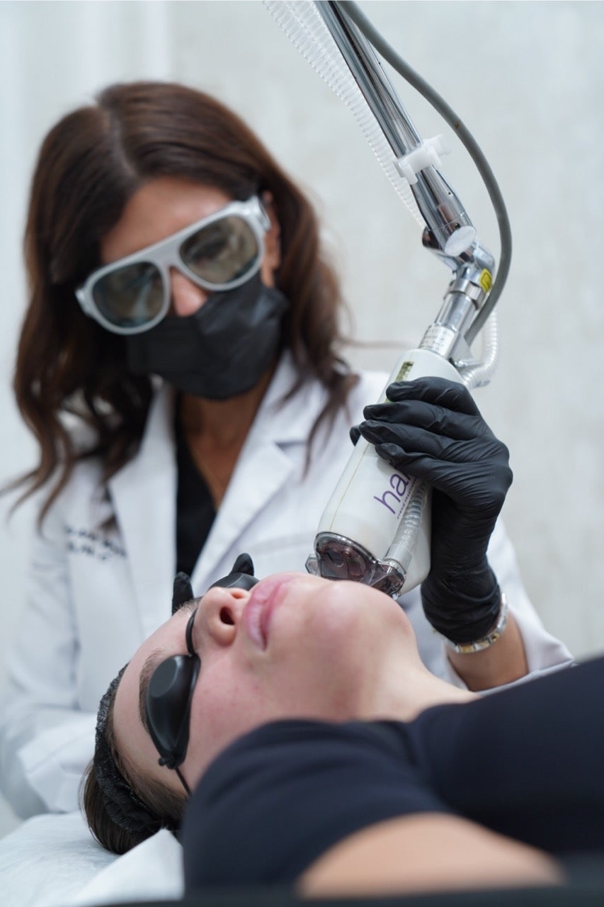  A professional using a laser to treat a woman 's face, who wears protective eye covers and has lines marked on her skin.