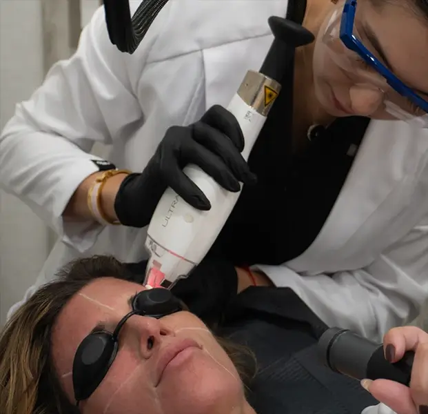 Patient receiving a cosmetic injection near her eyebrow from a gloved hand holding a syringe.