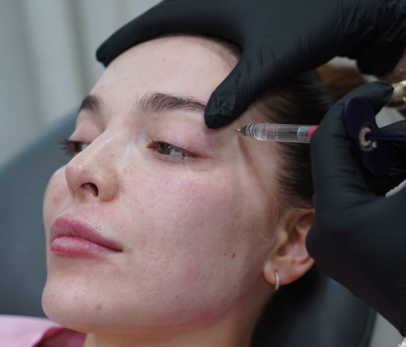 Close-up of a person receiving an injection near their eye from a doctor wearing black gloves.