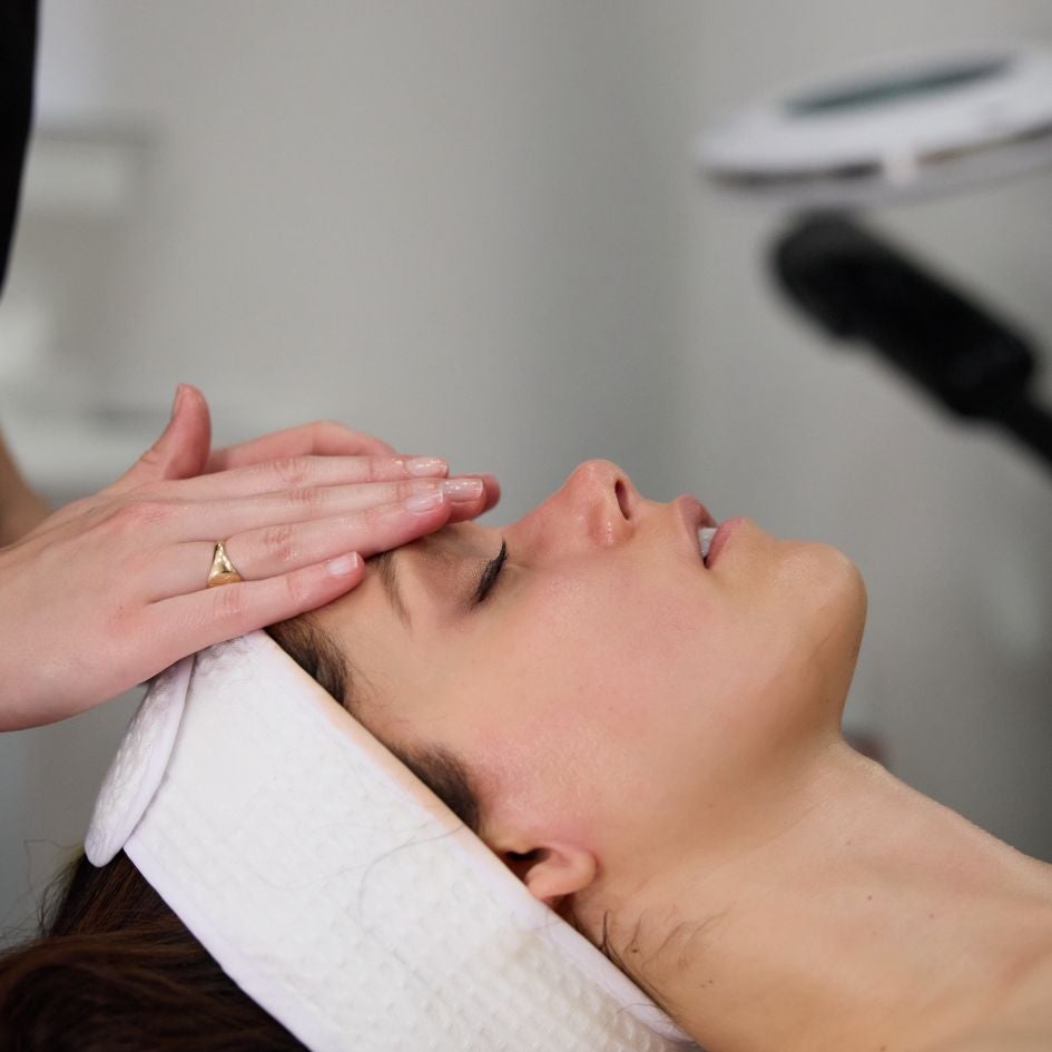 A woman in a white robe examines her face in a mirror while a doctor in a white coat adjusts her hair.