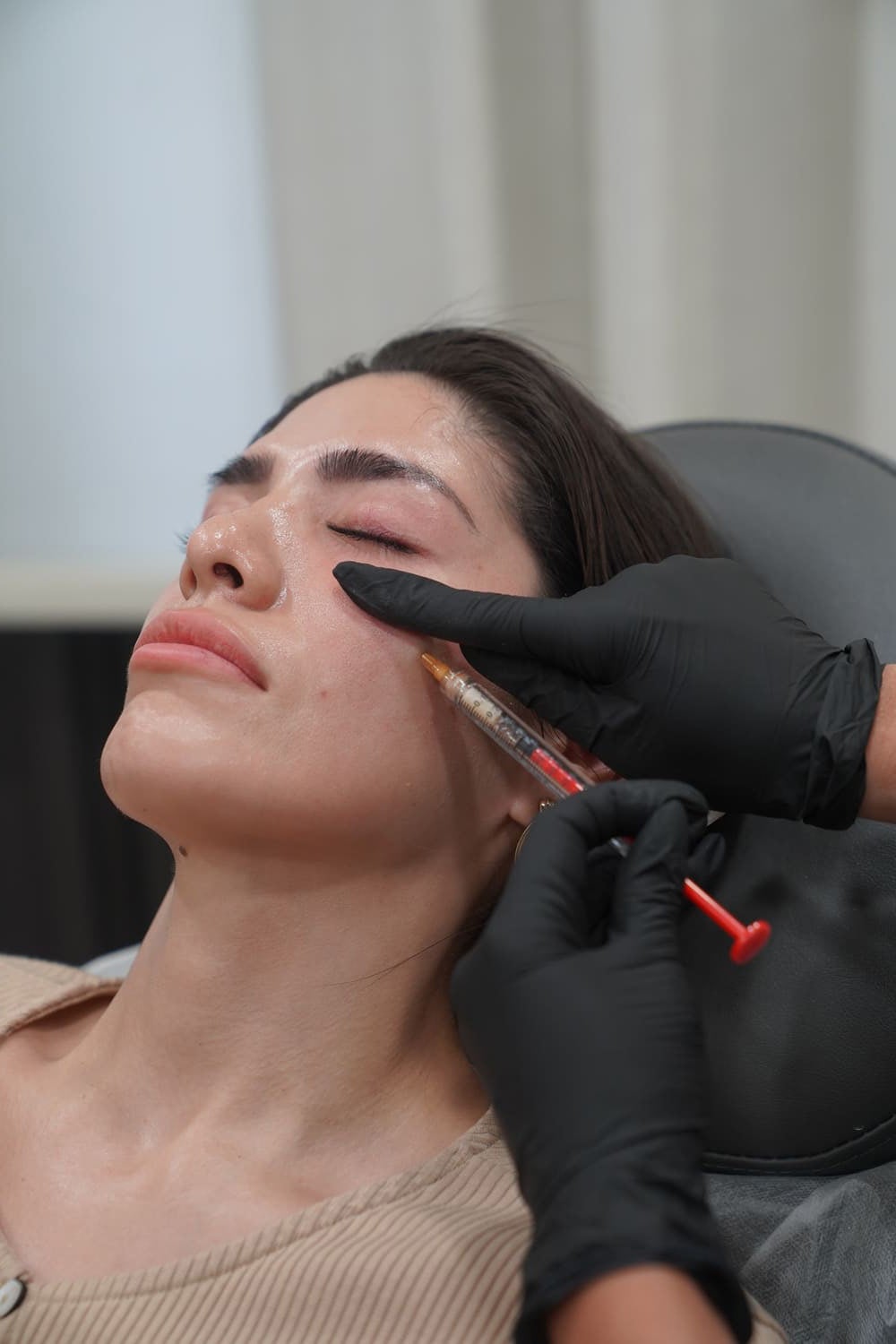 A woman getting an injection near her eye from a person in black gloves during a cosmetic procedure.