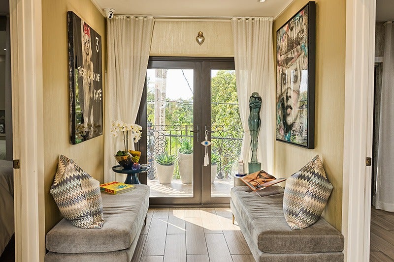 A stylish entryway with two grey velvet benches flanking double doors leading to a balcony with green foliage.