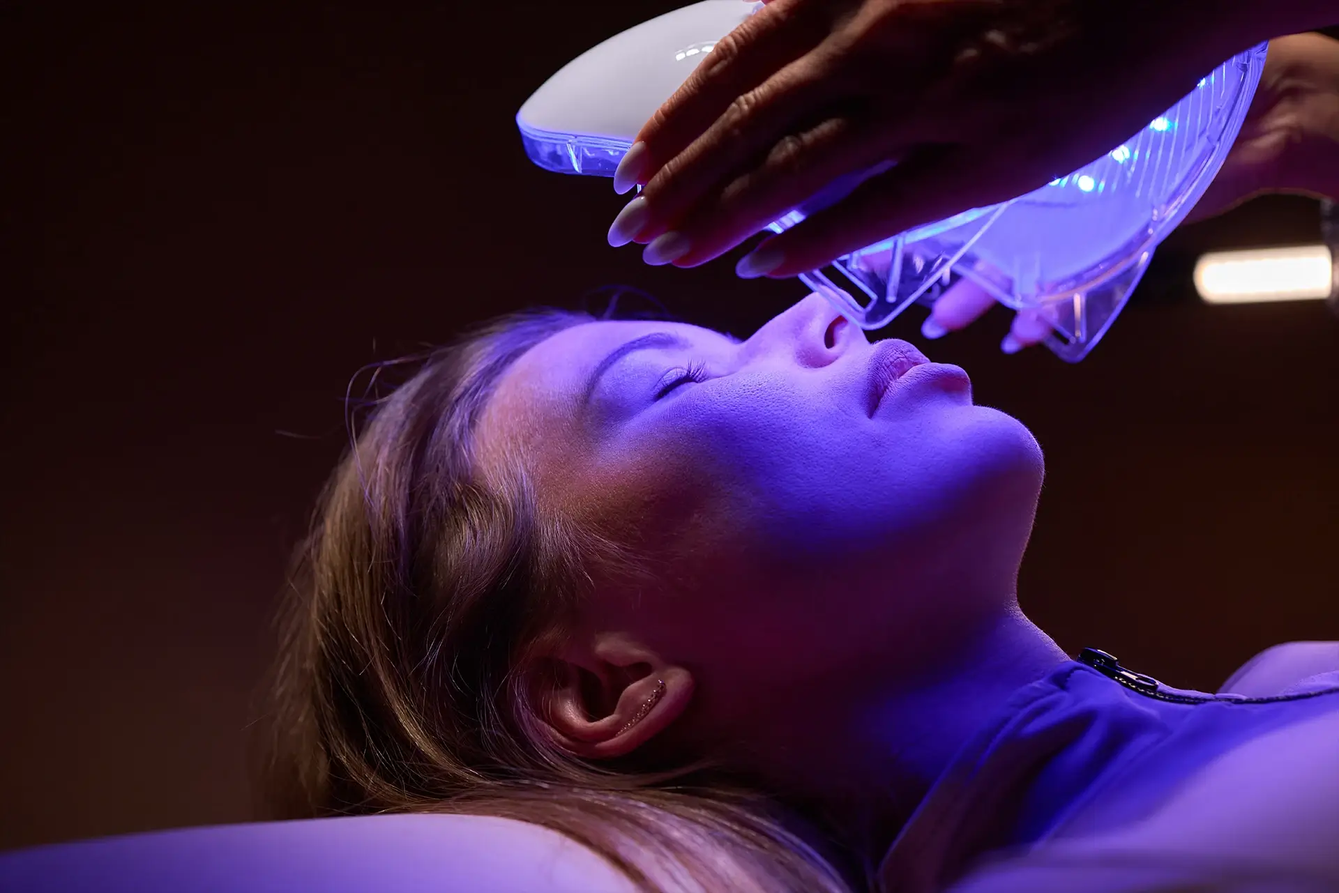 A person receiving blue light therapy on her face from a device held by an unseen person.